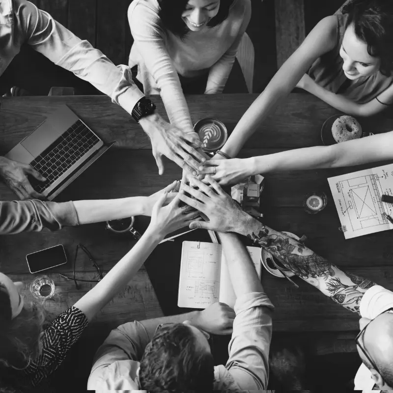 Mehrere Personen sitzen an einem Tisch und strecken Ihre hände in die Mitte als ein Team